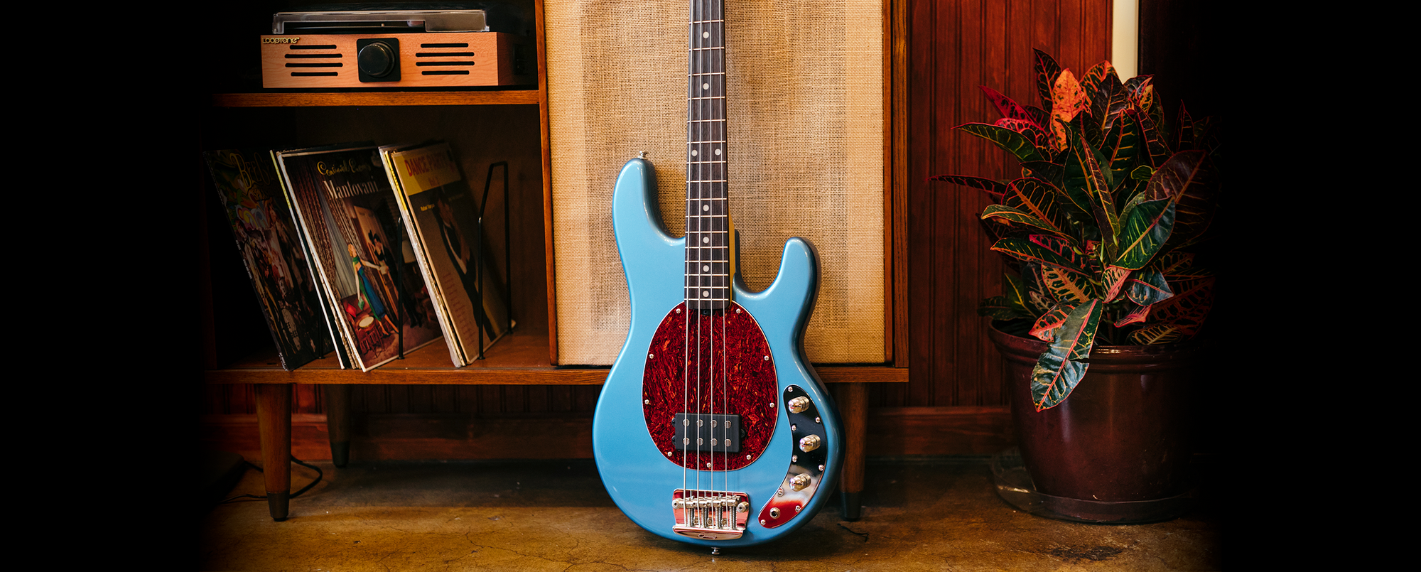 The StingRay Classic Ray25CA bass in Toluca Lake Blue resting against a mid century cabinet.